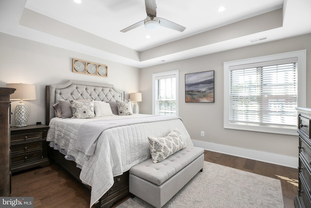 bedroom featuring dark hardwood / wood-style floors, a tray ceiling, multiple windows, and ceiling fan