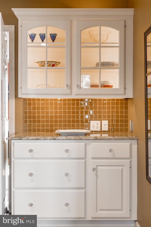 kitchen with backsplash, light stone countertops, and white cabinets