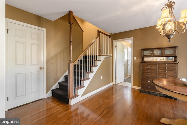 foyer entrance with baseboards, a notable chandelier, stairway, and wood finished floors