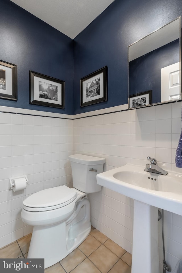 bathroom featuring tile patterned flooring, a wainscoted wall, tile walls, and toilet