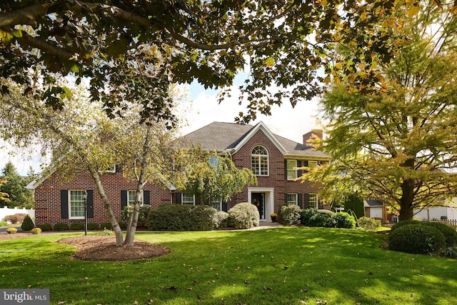 view of front of house with brick siding, a front lawn, and a chimney