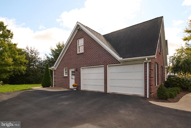 view of side of property with driveway, brick siding, roof with shingles, and an attached garage