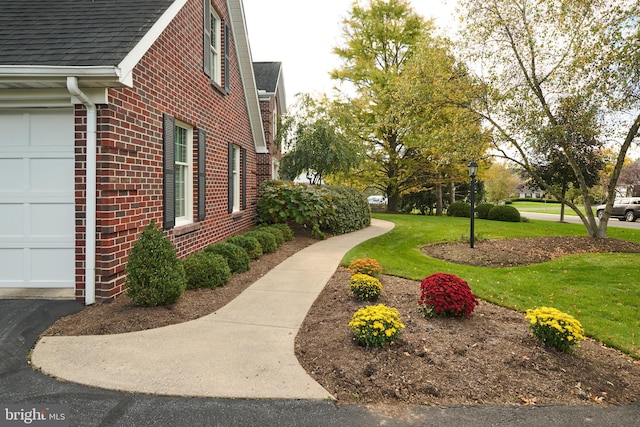 view of property exterior featuring a shingled roof, brick siding, a yard, and an attached garage