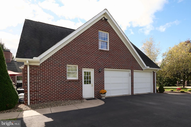 view of home's exterior with driveway, brick siding, and a shingled roof