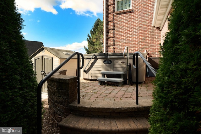 view of home's exterior with brick siding, an outdoor structure, a shed, a patio area, and a hot tub