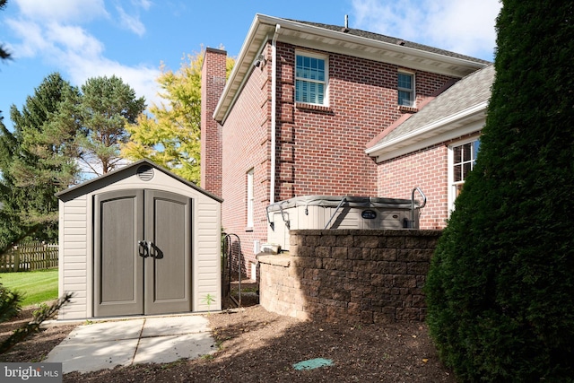 rear view of property featuring an outbuilding, brick siding, a chimney, a storage unit, and fence