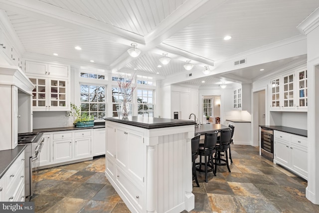 kitchen with a center island with sink, beamed ceiling, white cabinetry, a breakfast bar area, and beverage cooler