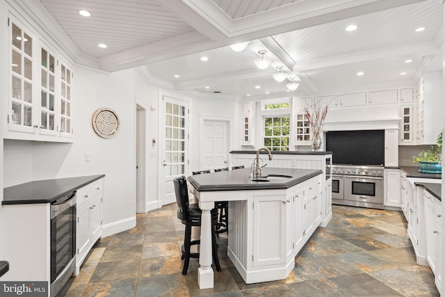 kitchen with a kitchen bar, beverage cooler, sink, a center island with sink, and white cabinets