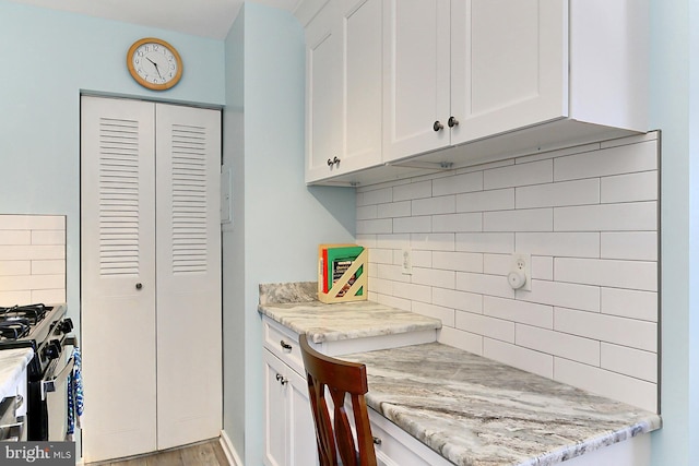 kitchen featuring backsplash, stainless steel range with gas cooktop, white cabinetry, and light stone countertops