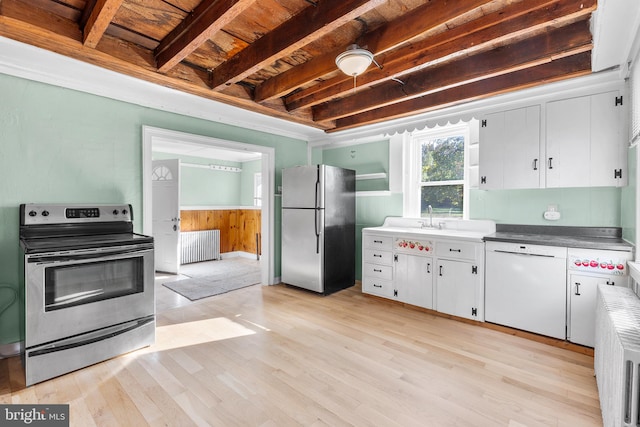 kitchen featuring light wood-type flooring, radiator heating unit, white cabinetry, stainless steel appliances, and beamed ceiling