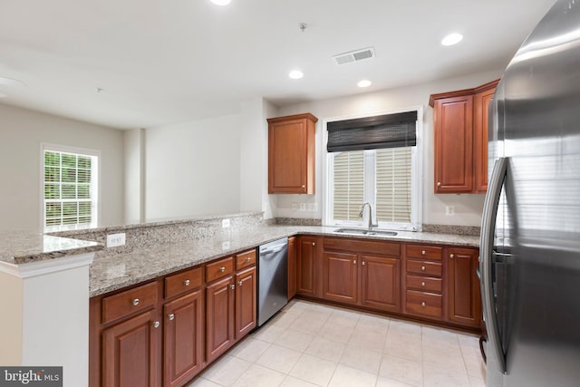 kitchen featuring stainless steel appliances, kitchen peninsula, light stone countertops, and sink