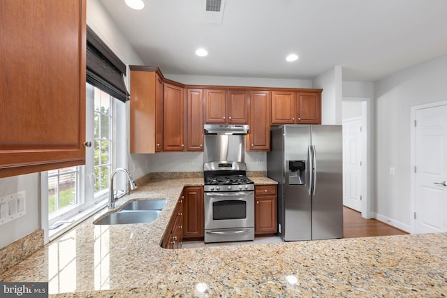 kitchen with appliances with stainless steel finishes, light wood-type flooring, light stone countertops, and sink