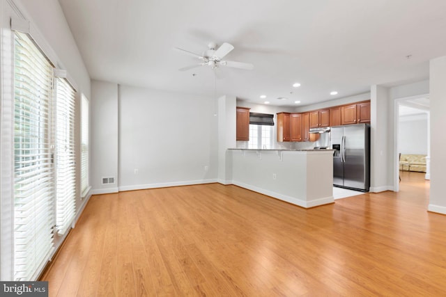 interior space with ceiling fan, stainless steel fridge, kitchen peninsula, light hardwood / wood-style flooring, and a kitchen breakfast bar