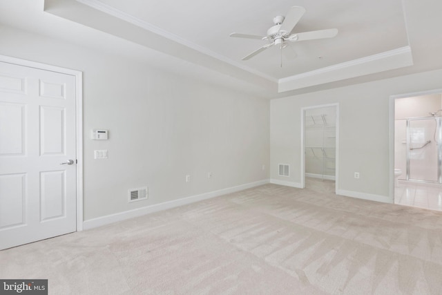 unfurnished bedroom featuring ceiling fan, a tray ceiling, a spacious closet, light carpet, and ensuite bath