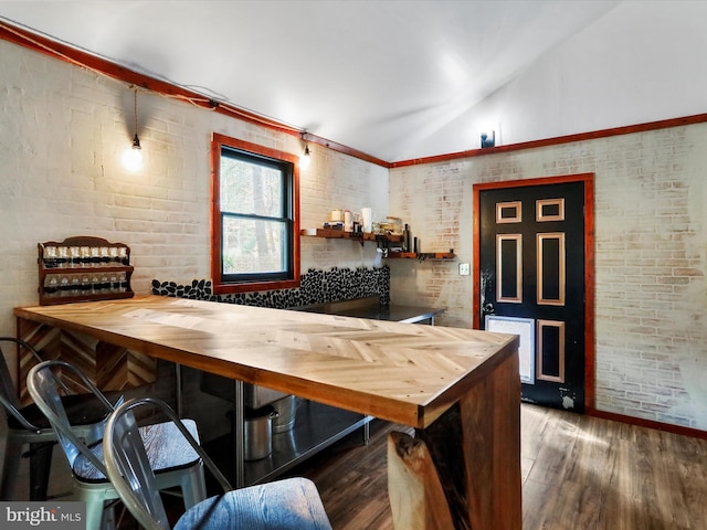 bar featuring wooden counters, brick wall, dark wood-type flooring, and vaulted ceiling