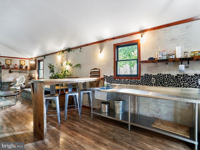 kitchen with stainless steel counters, lofted ceiling, dark hardwood / wood-style flooring, and brick wall