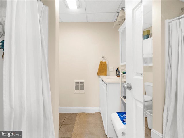 bathroom with toilet, tile patterned flooring, a paneled ceiling, heating unit, and vanity