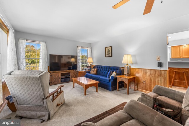 living room featuring ceiling fan, wooden walls, and light colored carpet