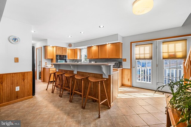 kitchen with wood walls, black oven, a center island, and a kitchen bar