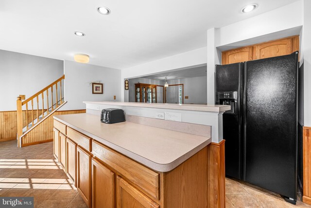 kitchen featuring wood walls, light tile patterned floors, a kitchen island, and black fridge with ice dispenser