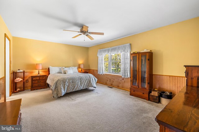 carpeted bedroom with ceiling fan and wooden walls