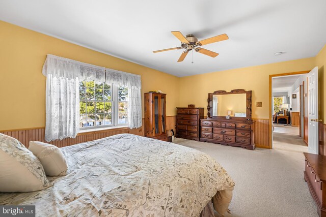 bedroom featuring ceiling fan, wood walls, and light carpet