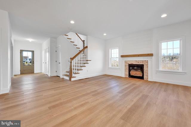 unfurnished living room featuring a brick fireplace, light hardwood / wood-style flooring, and a wealth of natural light