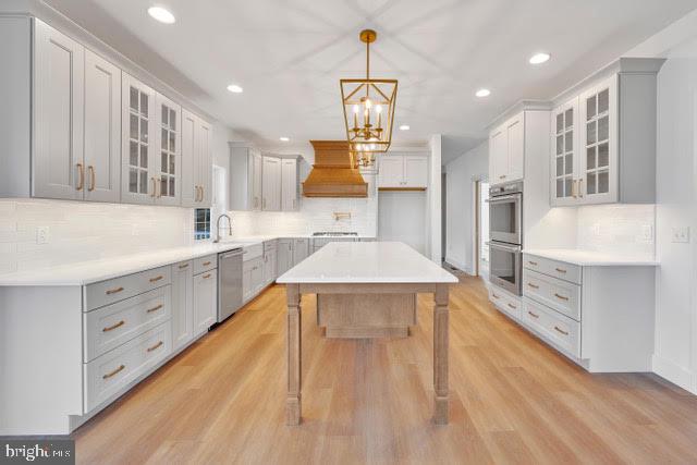 kitchen featuring backsplash, light wood-type flooring, stainless steel appliances, and hanging light fixtures