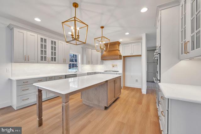 kitchen with pendant lighting, backsplash, custom range hood, a center island, and light hardwood / wood-style floors