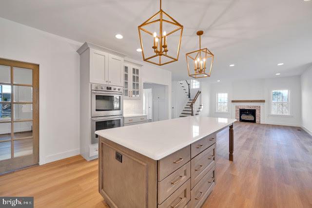 kitchen with white cabinets, pendant lighting, a kitchen island, light hardwood / wood-style flooring, and stainless steel double oven