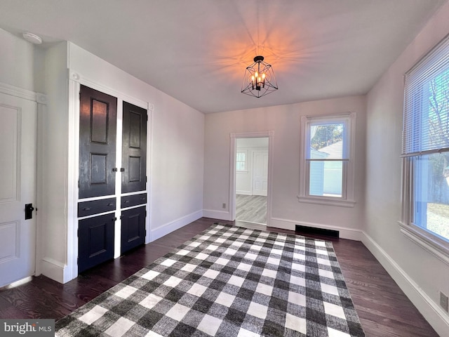 unfurnished dining area with plenty of natural light, baseboards, a notable chandelier, and dark wood finished floors