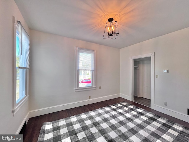 unfurnished dining area with baseboards, a notable chandelier, and dark wood-type flooring