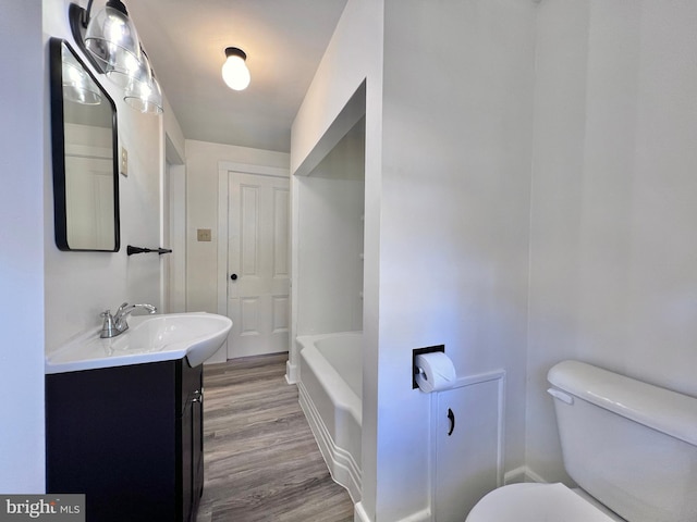 full bath featuring wood finished floors, a bathtub, vanity, and toilet