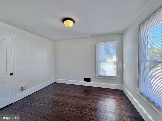 unfurnished room with baseboards, visible vents, and dark wood-style floors