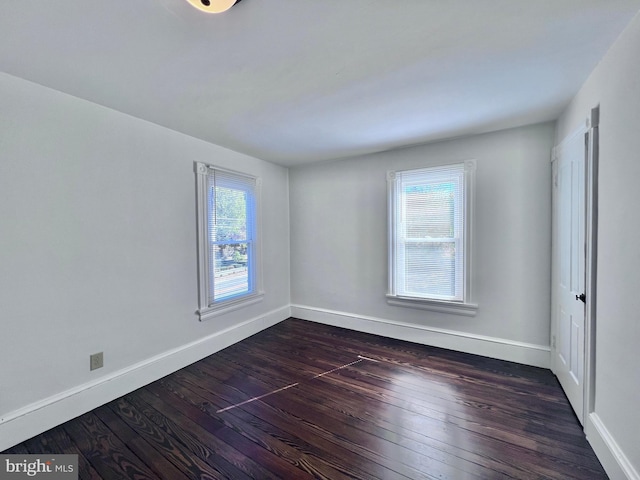 empty room featuring baseboards, dark wood-type flooring, and a healthy amount of sunlight