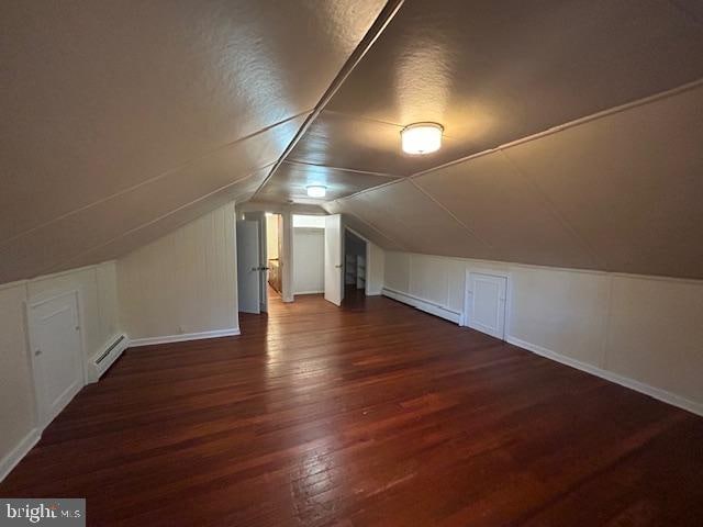 additional living space featuring dark hardwood / wood-style floors, a textured ceiling, baseboard heating, and vaulted ceiling