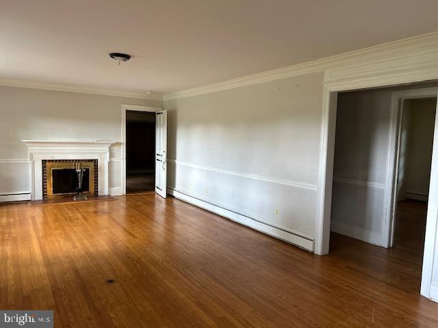 unfurnished living room with a baseboard heating unit, a fireplace, dark hardwood / wood-style flooring, and crown molding