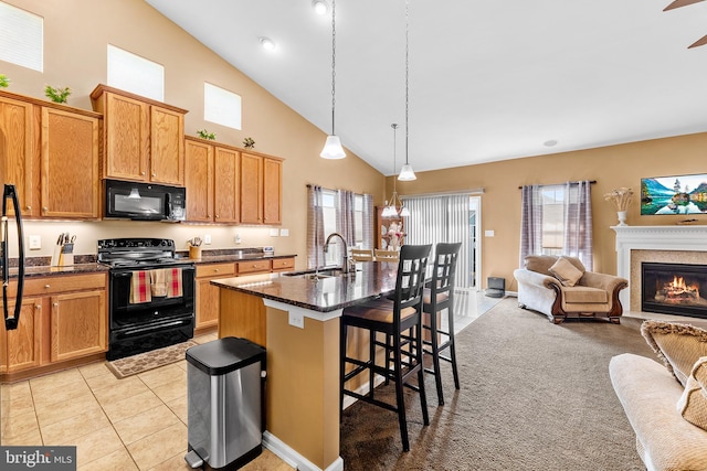 kitchen with a kitchen breakfast bar, a center island with sink, sink, black appliances, and pendant lighting