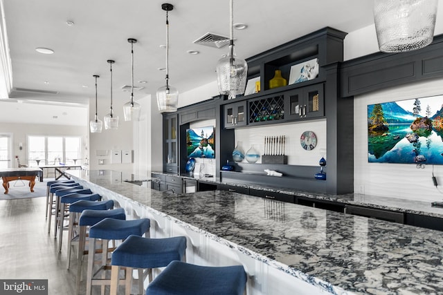 kitchen with pool table, dark stone countertops, hanging light fixtures, and a kitchen bar