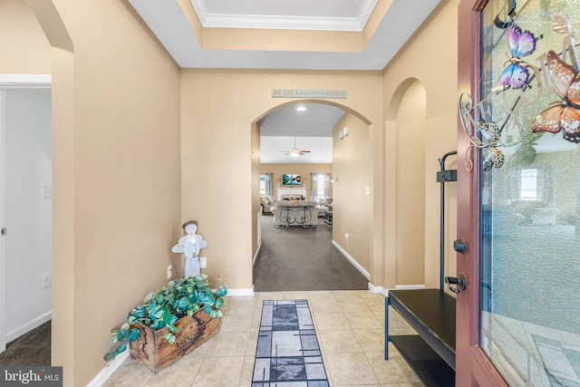 hall with light carpet, crown molding, and a tray ceiling