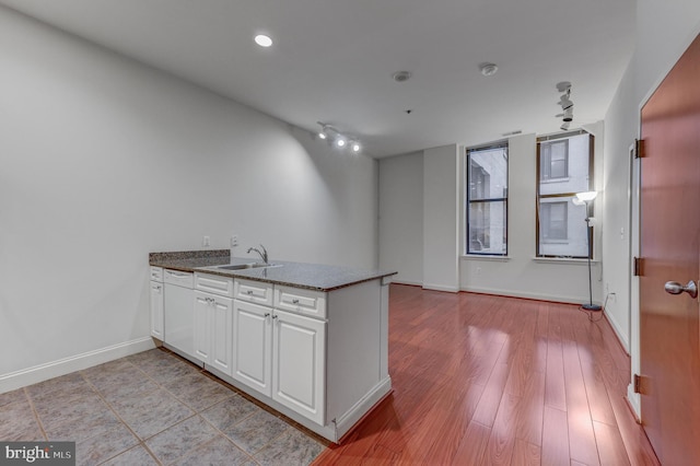 kitchen featuring kitchen peninsula, sink, dark stone countertops, white cabinets, and light hardwood / wood-style floors