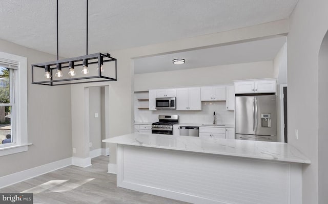 kitchen with pendant lighting, sink, light stone countertops, appliances with stainless steel finishes, and white cabinetry