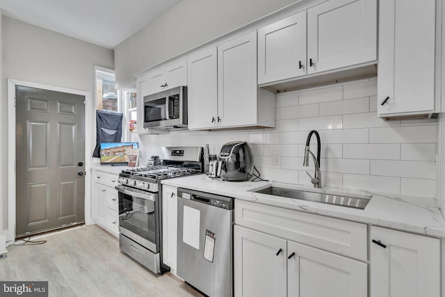 kitchen featuring sink, stainless steel appliances, light stone counters, light hardwood / wood-style floors, and white cabinets