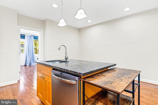 kitchen featuring sink, an island with sink, pendant lighting, stainless steel dishwasher, and light hardwood / wood-style flooring