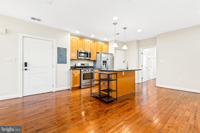 kitchen featuring a kitchen island with sink, a breakfast bar area, hanging light fixtures, stainless steel appliances, and wood-type flooring