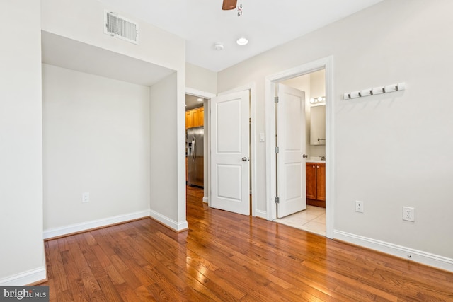 unfurnished bedroom featuring light hardwood / wood-style flooring, stainless steel refrigerator with ice dispenser, connected bathroom, and ceiling fan