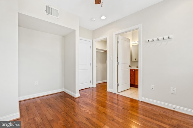 unfurnished bedroom with light hardwood / wood-style floors, a closet, connected bathroom, and ceiling fan