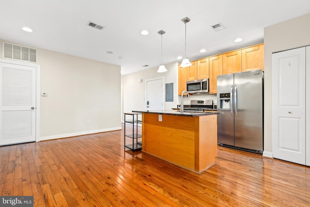 kitchen featuring light brown cabinets, appliances with stainless steel finishes, a kitchen island with sink, a kitchen bar, and light hardwood / wood-style flooring