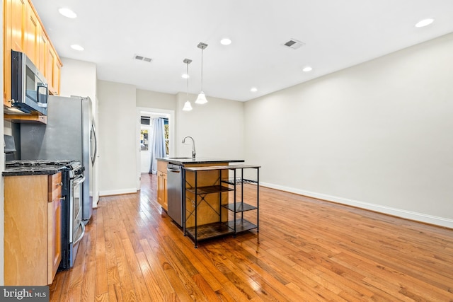 kitchen with hanging light fixtures, an island with sink, appliances with stainless steel finishes, a kitchen breakfast bar, and light hardwood / wood-style flooring