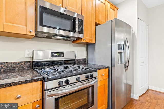 kitchen with dark stone countertops, stainless steel appliances, and light wood-type flooring